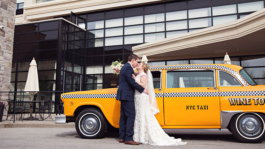 bride and groom kissing in front of old yellow taxi in front of the C Hotel by Carmen's