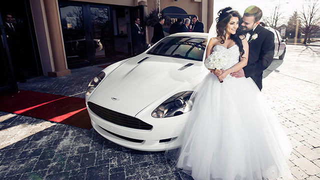 bride and groom pose outside of Carmen's Banquet Centre in front of white sports car
