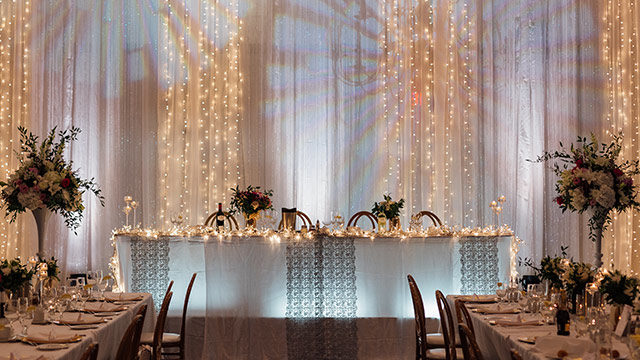 head table with twinkle lights, white linens and floral centerpieces at Carmen's
