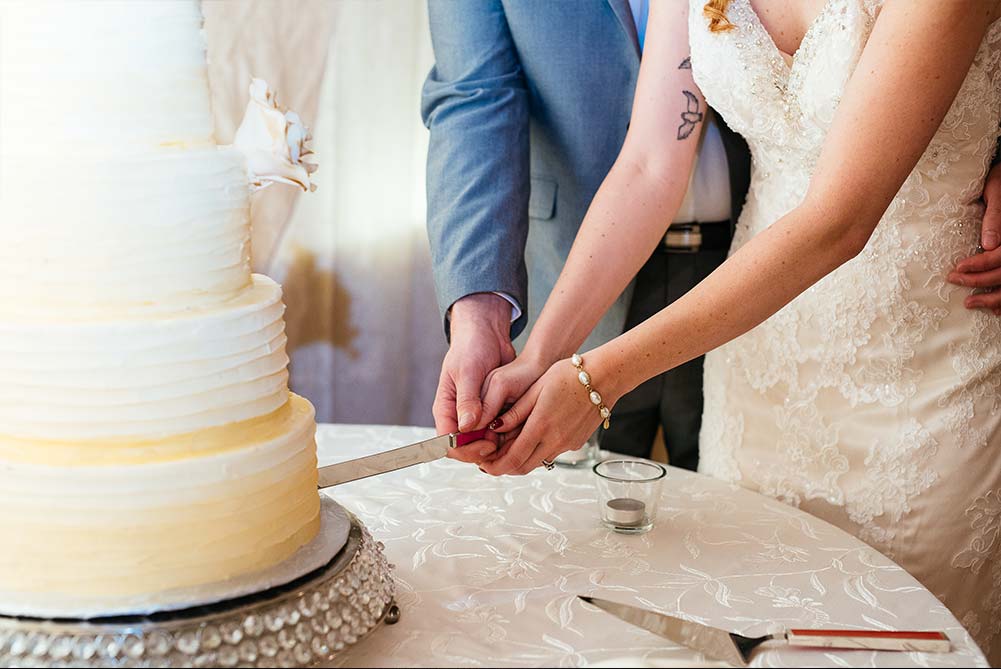 closeup of bride and groom holding hands as they cut wedding cake