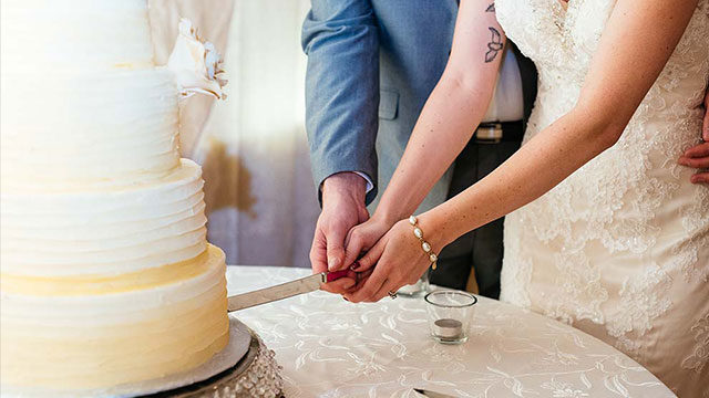 closeup of bride and groom holding hands as they cut wedding cake
