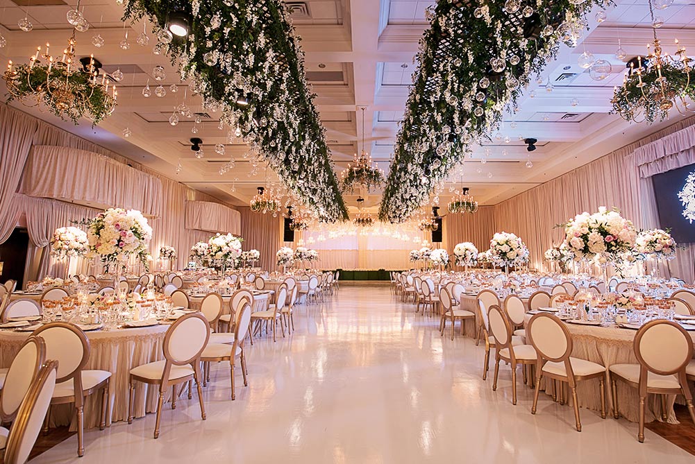 ivory wedding decor in ballroom at Carmen's with hanging florals and gold King Louie chairs