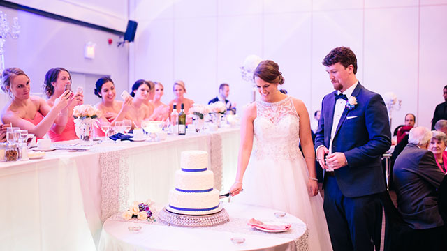 bride and groom cutting wedding cake as bridal party takes photos