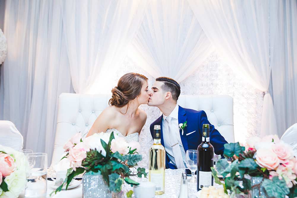 bride and groom kissing at head table during wedding at Carmen's