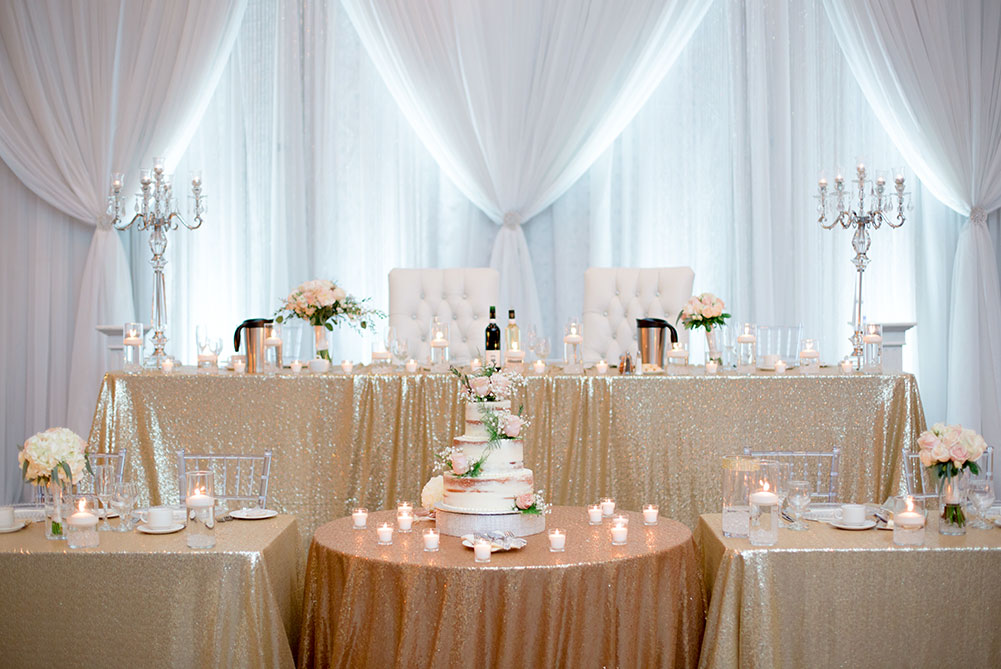 view of head table with gold sequin linens and acrylic chiavari chairs