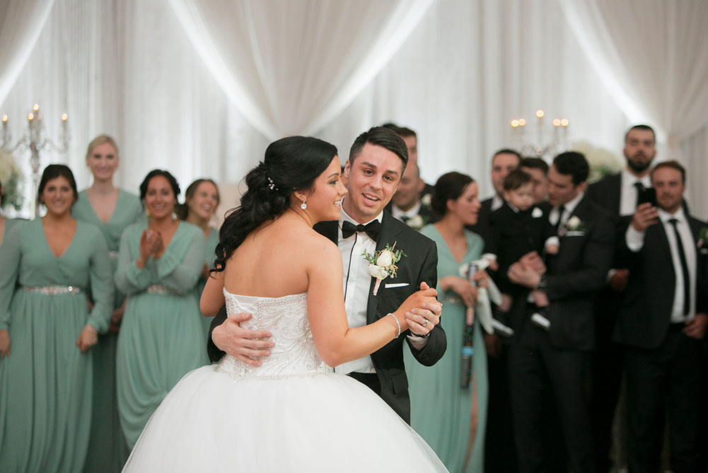 bride and groom having first dances as bridal party watches