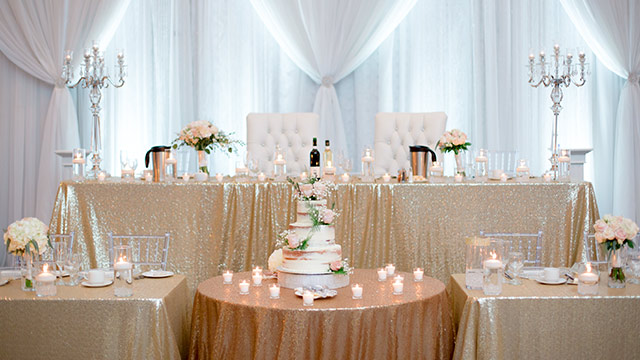 view of head table with gold sequin linens and acrylic chiavari chairs
