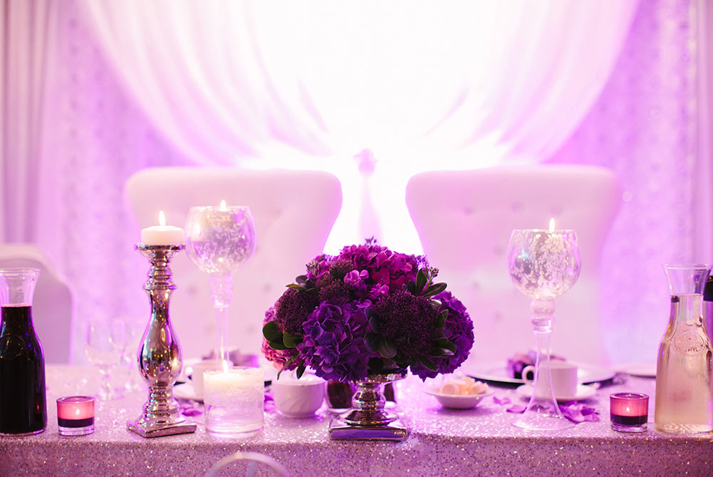close up of purple head table decor with white king and queen chairs