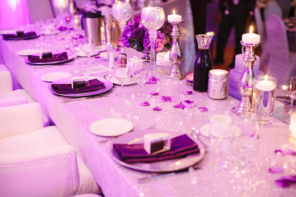 close up of wedding table decor showing purple sequin linens, silver candle holders and purple flower petals